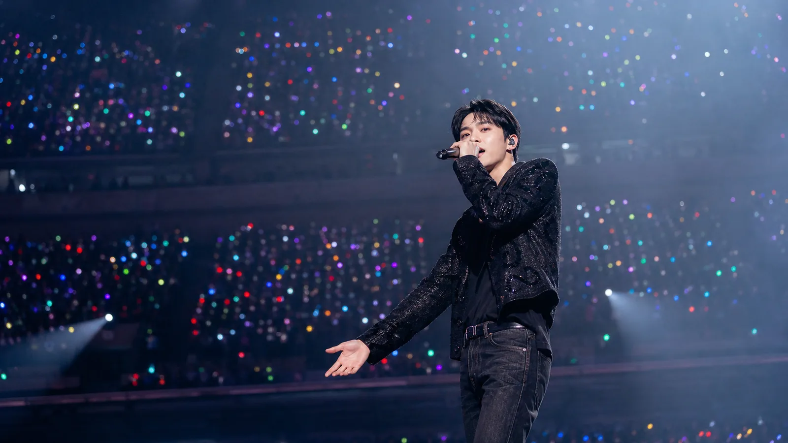 A performer on an arena stage, the crowd behind them filled with glowing light sticks