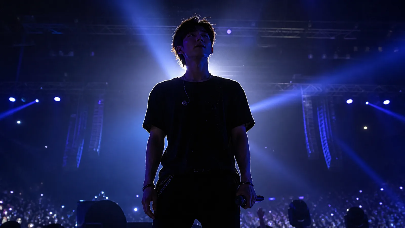 A performer silhouetted against blue stage lights, holding a microphone